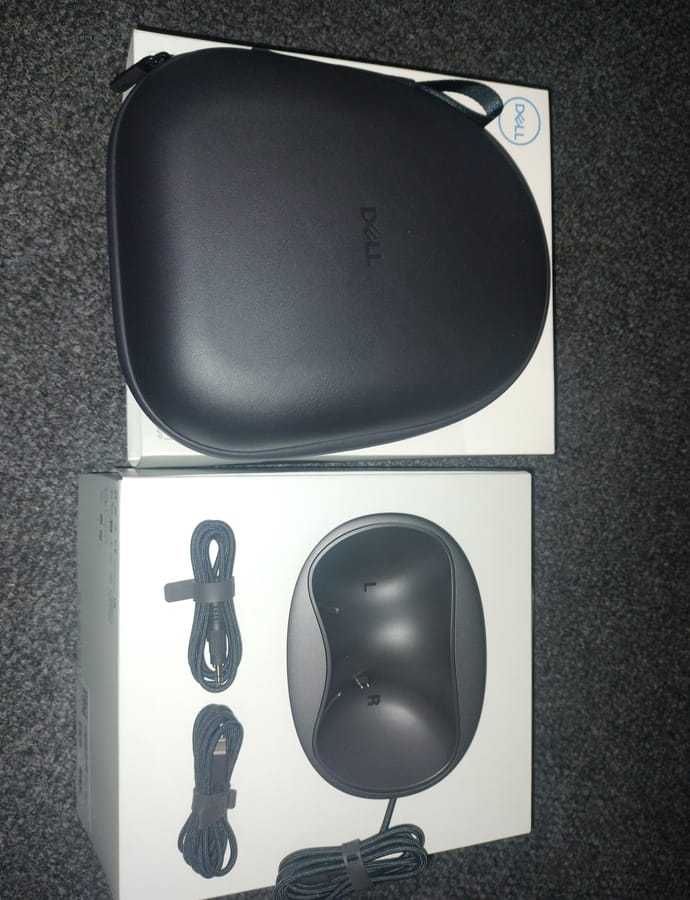 The Dell WL7024 hard case alongside the retail box panel showing the charging stand with left and right cradles, a braided USB cable and a braided audio cable