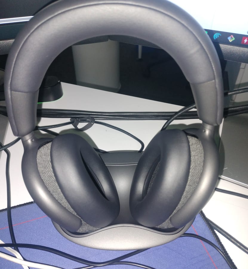 Dell WL7024 headset resting on its charging stand on a desk, with the fabric-trimmed ear cups facing forward